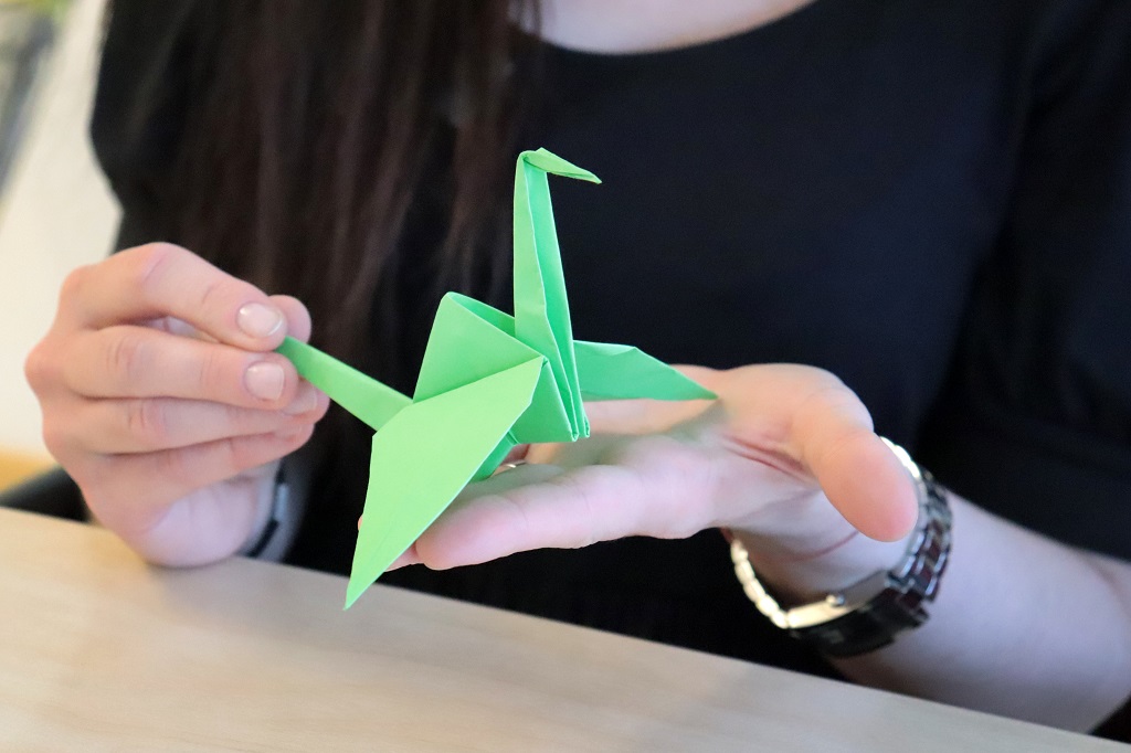 dz12 Rokās tur no zaļa papīra izveidotu dzērves origami