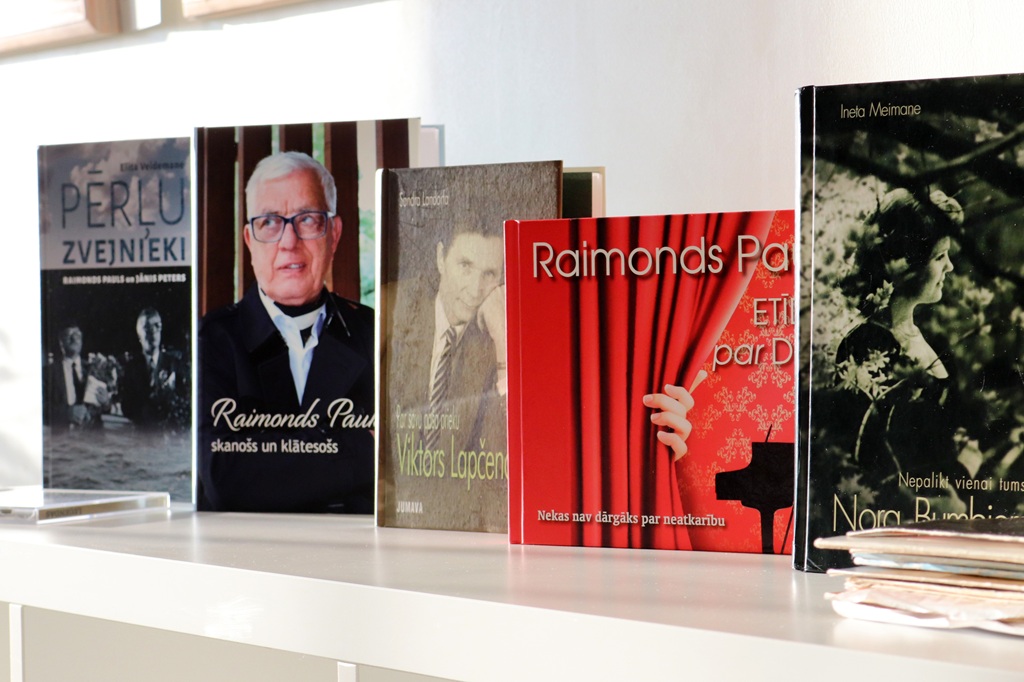 Koka plaukts, kas piepildīts ar dažādām grāmatām, demonstrējot dažādu krāsu un izmēru gammu.