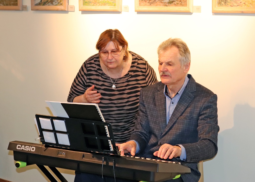 Vīrietis un sieviete kopā priecīgi spēlē elektronisko klavieru mājīgā vidē.