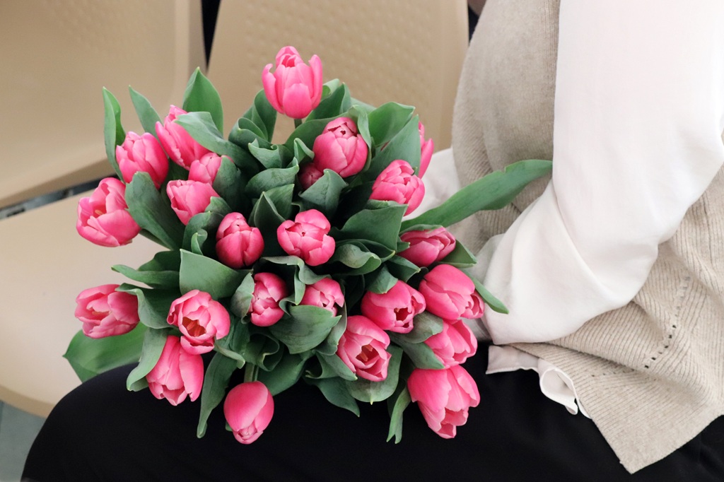 Sieviete tur rokās košu rozā tulpju pušķi, izceļot to smalkās ziedlapiņas un svaigos zaļumus.