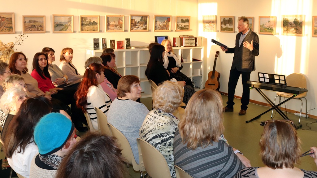 Cilvēku grupa, kas sēž krēslos un uzmanīgi klausās vīrieša runā prezentācijā vai sanāksmē.