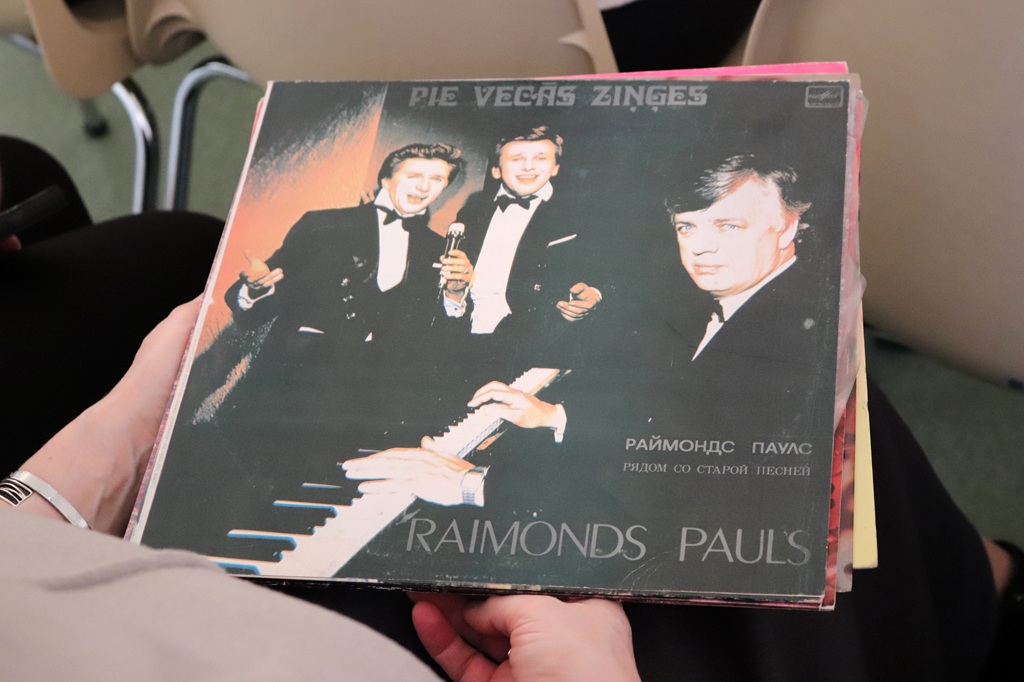 Cilvēks tur rokās skaņu plati, uz kuras vāka ir attēloti divi vīrieši.