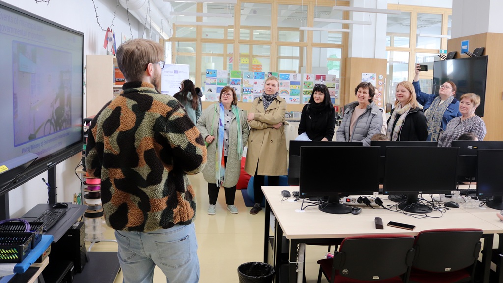 Persona maskēšanās žaketē uzstājas ar prezentāciju uzmanīgiem pieaugušajiem datorlaboratorijā. Atmosfēra ir izglītojoša un aizraujoša.