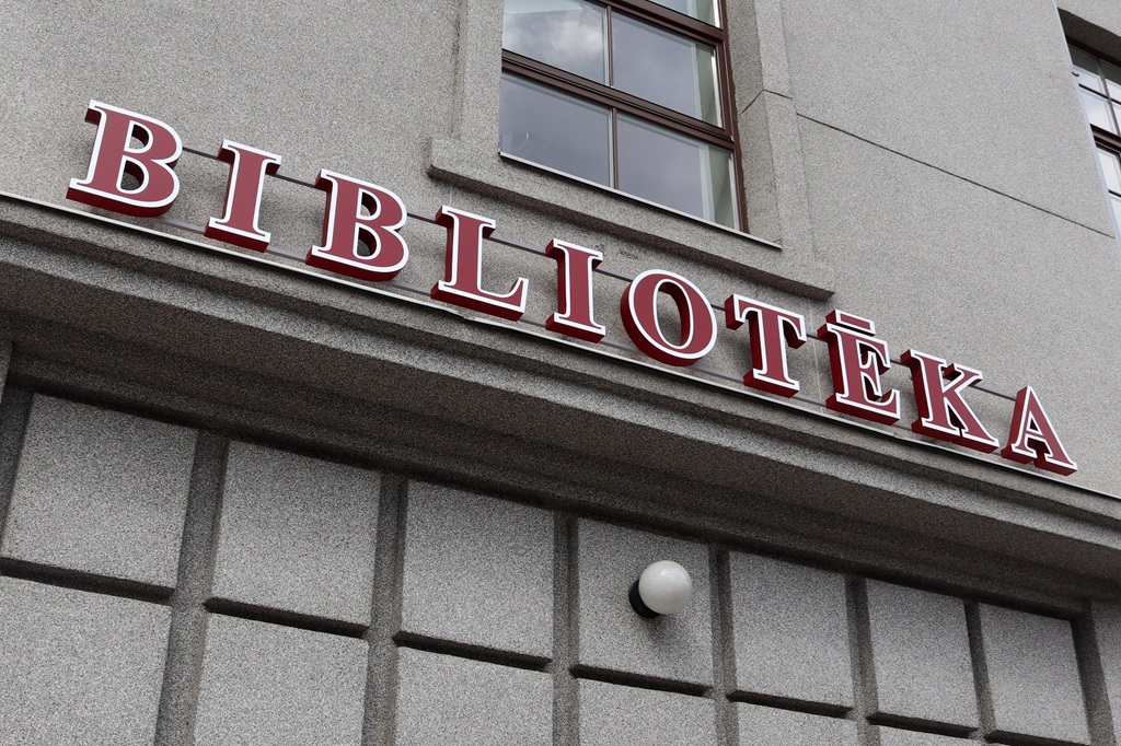 Ēkas eksterjers ar lieliem, sarkaniem burtiem uzrakstu “BIBLIOTĒKA”.