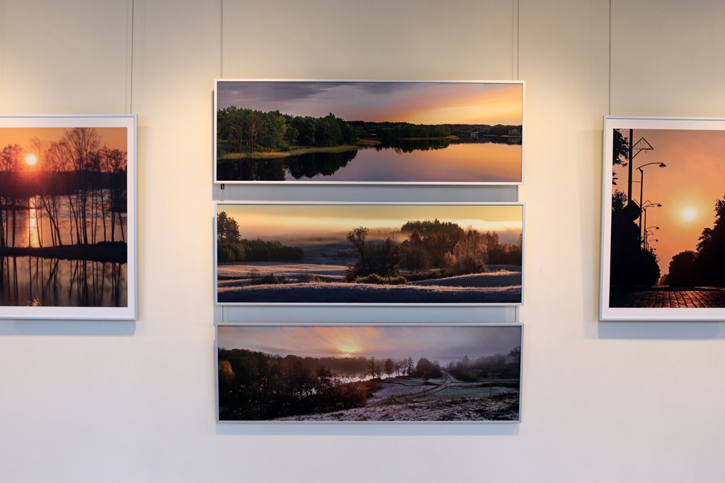 Galerijas sienā ir izvietotas piecas ierāmētas ainavu fotogrāfijas, kurās redzami mierīgi saulrieti virs ezeriem, apledojuši lauki un ar kokiem apaugusi iela, radot mieru.