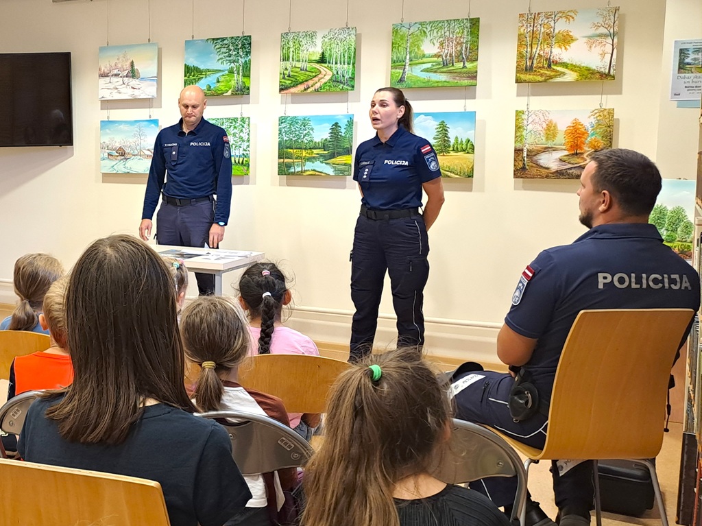 Policijas darbinieki mākslas galerijā prezentē izrādi vērīgu bērnu grupai. Sienas rotā krāsainas ainavu gleznas, radot izglītojošu un pozitīvu atmosfēru.