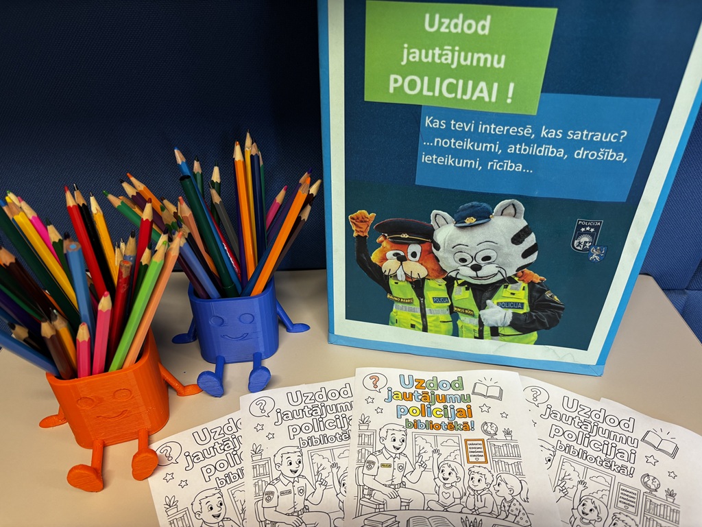Krāsaini zīmuļi animētos turētājos blakus plakātam, kurā attēloti dzīvnieku tēli policistu tērpos, ar brošūrām priekšplānā. Tonis ir rotaļīgs un saistošs.