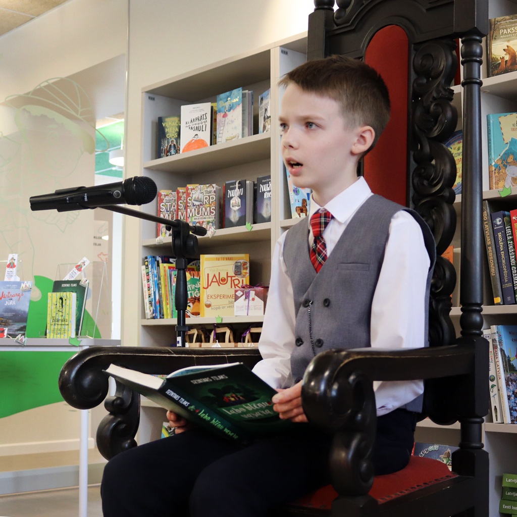 Zēns lasa no grāmatas bibliotēkas vidē.