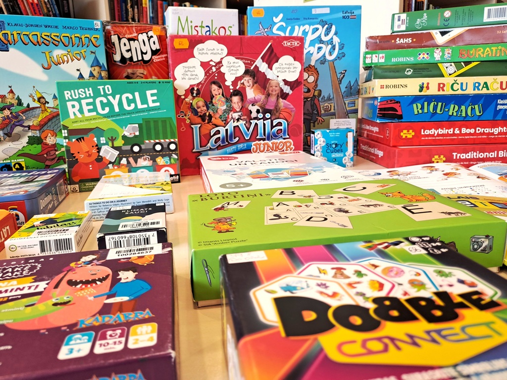 Bagātīgs galda un prāta spēļu klāsts novietots stateniski un guļus uz galda, tostarp "Carcassonne Junior", "Jenga", "Latvija Junior" un "Dooble Connect", kas sagatavots bērnu tematisko spēļu dienai bibliotēkā.