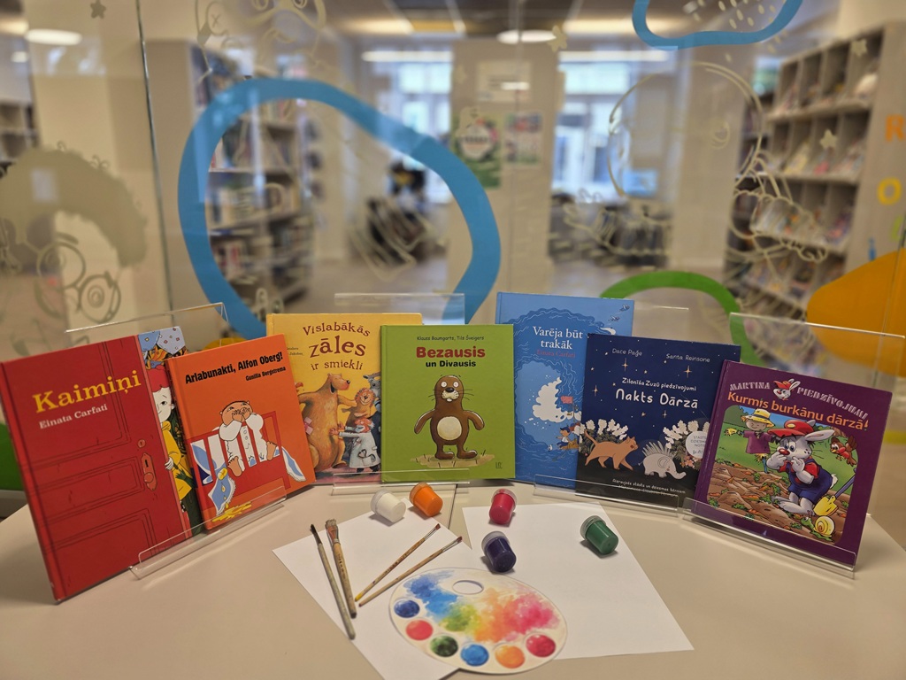 Bērnu grāmatu izstāde bibliotēkā uz galda ar krāsām, otām un mākslinieka paleti