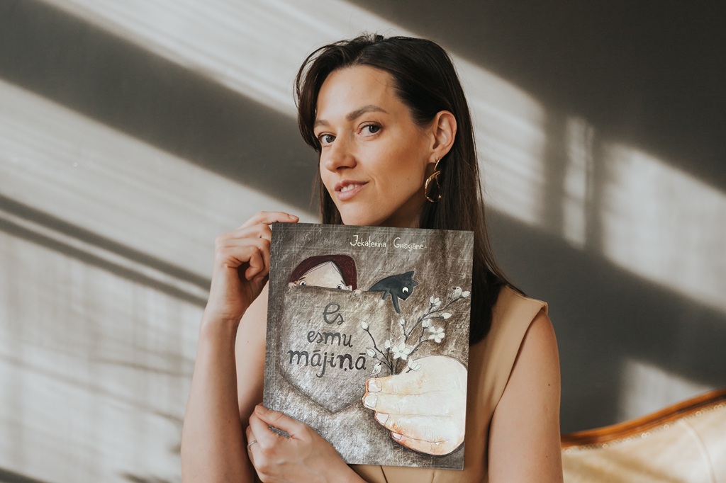 Daugavpils bērnu grāmatu autore un ilustratore Jekaterina Griškjāne smaida, turot rokās savu grāmatu 'Es esmu mājiņā', kas nominēta Jāņa Baltvilka balvai grāmatu mākslā.