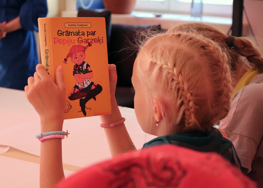 Meitene tur rokās grāmatu "Grāmata par Pepiju Garzeķi" un uzmanīgi pēta Pepijas tēlu.