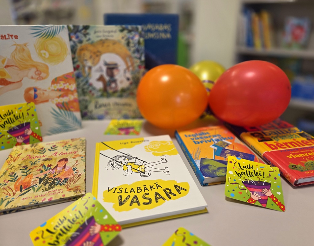 Bērnu grāmatu izstāde bibliotēkā uz galda ar krāsainiem gaisa baloniem un kartītēm "Laiks ballītei!"