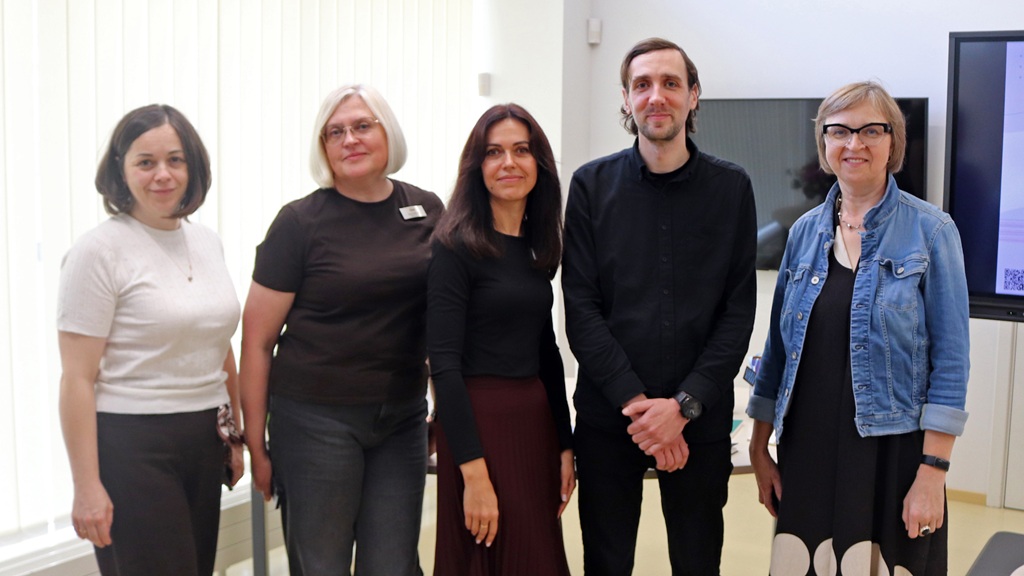 Pasākuma rīkotāju un runātāja kopīgais fotoattēls bibliotēkas telpā