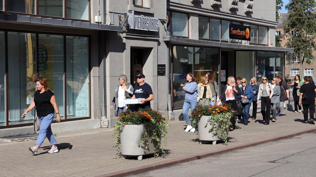Gājēju grupa pastaigājas gar Vienības nama ēku Daugavpils centrā.