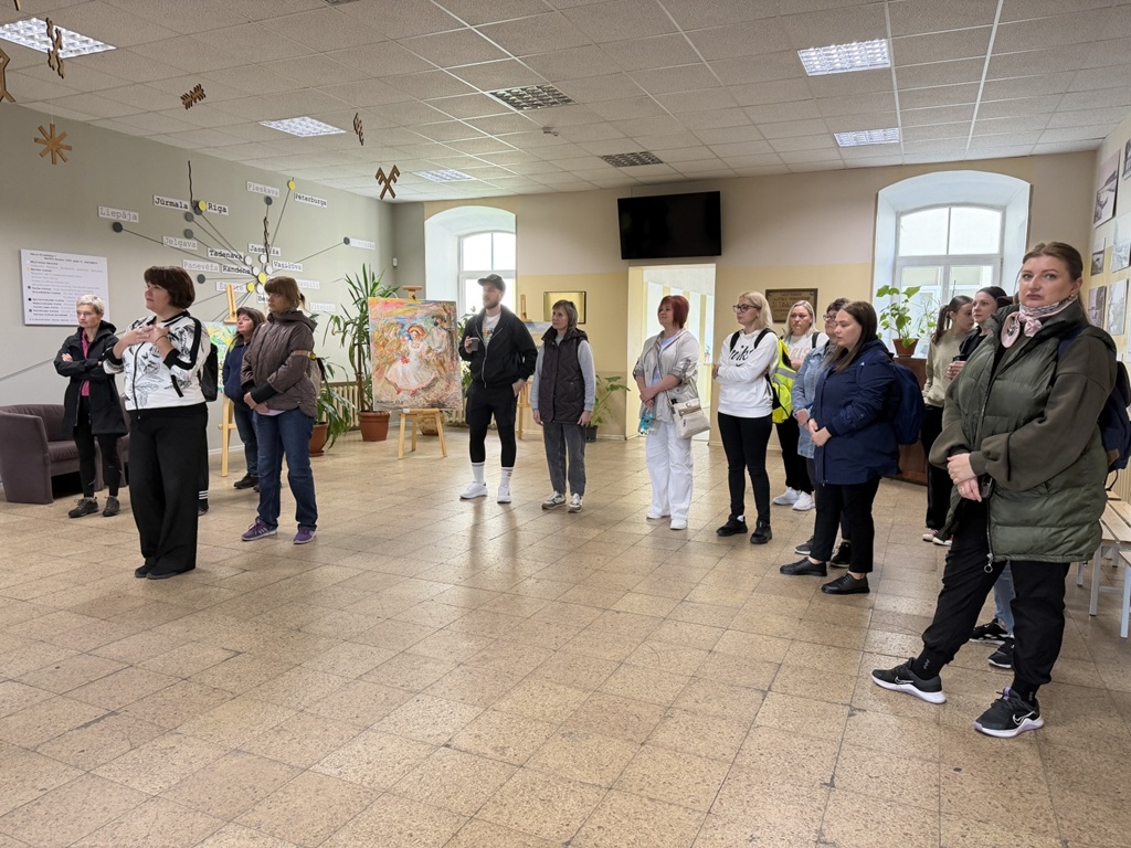Apmeklētāju grupa sapulcējusies plašā izstāžu zālē kultūras pasākuma laikā