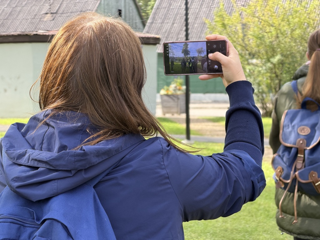 Sieviete no mugurpuses fotografē ar viedtālruni āra vidē