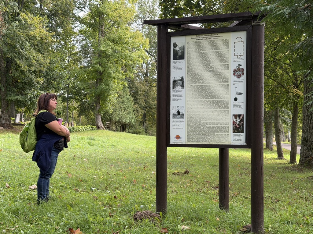 Sieviete lasa informācijas stendu par Birķineļu luterāņu baznīcas drupām