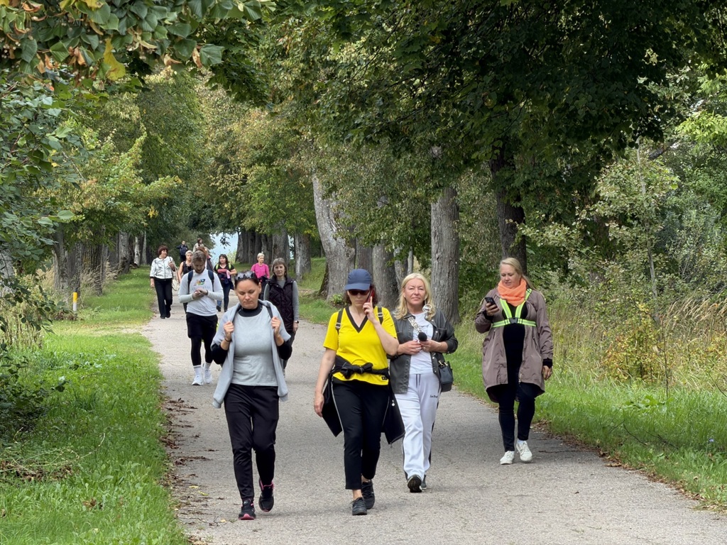 Cilvēki iet pa koku aleju dabas takā