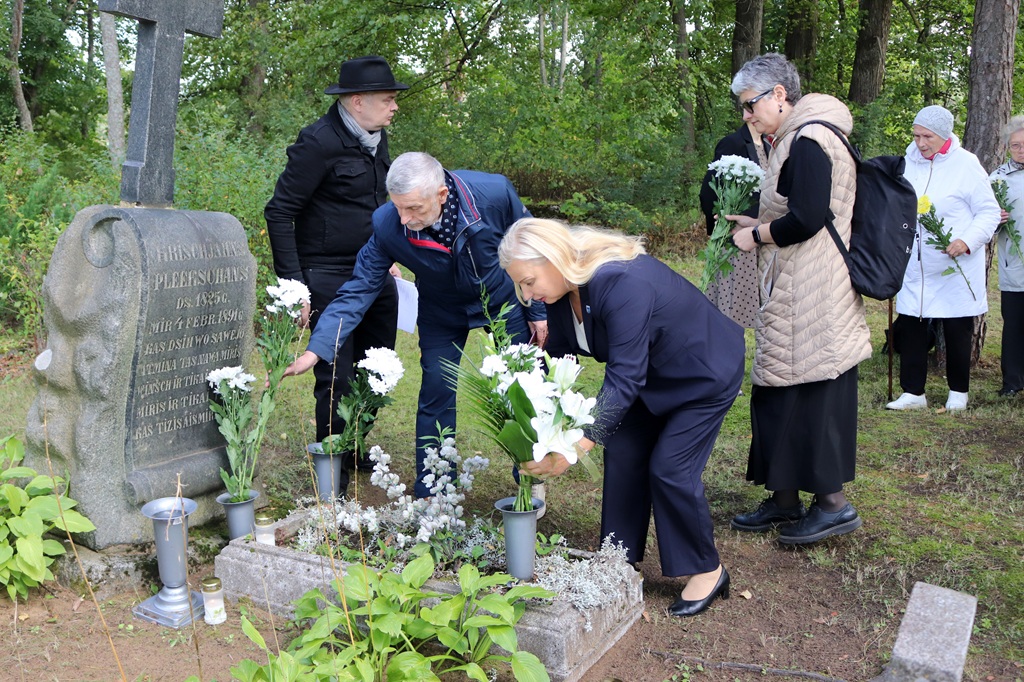 Sieviete un vīrietis noliek baltu ziedu pušķus pie akmens kapa pieminekļa kapsētā