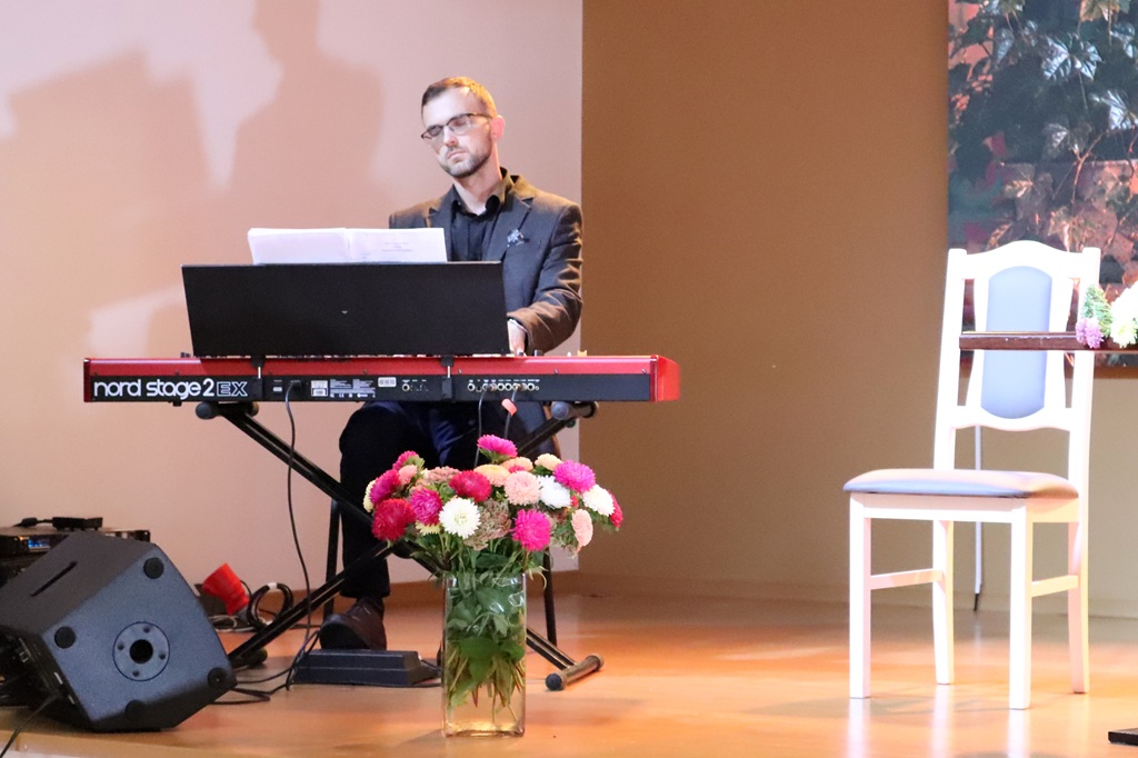 Pianists uzstājas pie sarkanā sintezatora uz skatuves pasākuma laikā