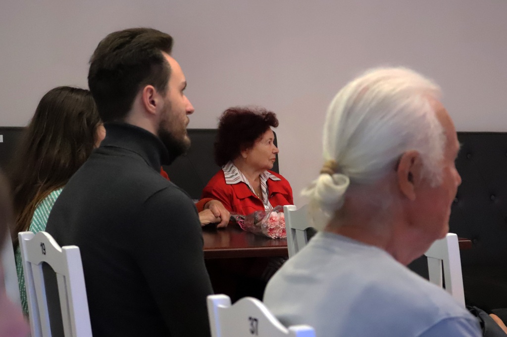 Pasākuma apmeklētāji sēž skatītāju rindās un uzmanīgi vēro priekšnesumu