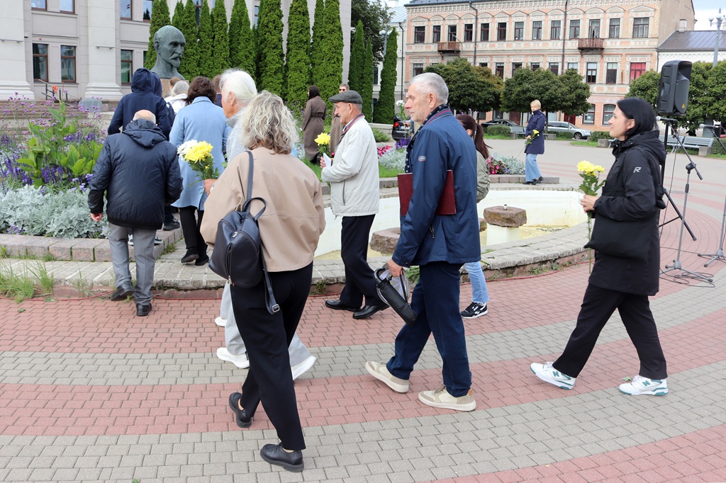 Pasākuma dalībnieki ar ziediem rokās dodas nolikt ziedus pie pieminekļa