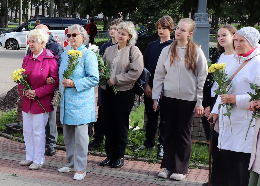 Pasākuma dalībnieki un apmeklētāji ar ziediem rokās stāv parkā