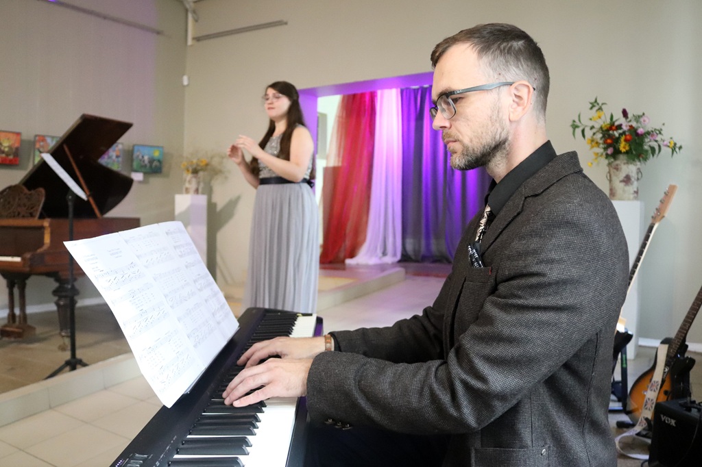 Pianists tuvplānā spēlē klavieres dziedātājas priekšnesuma laikā