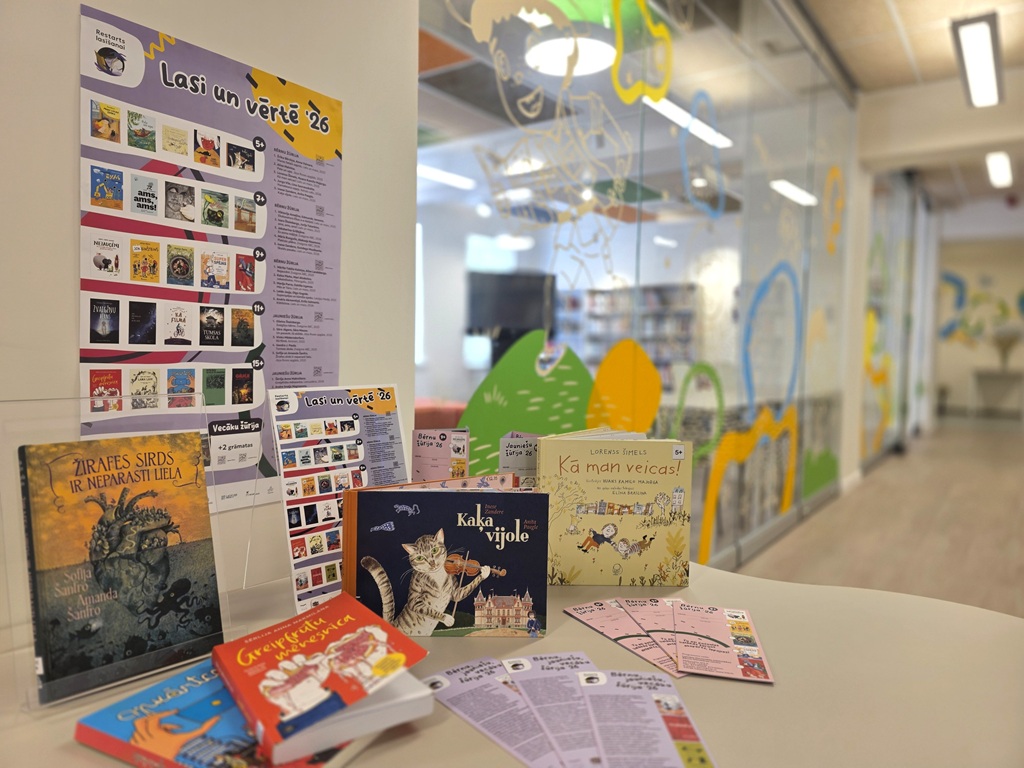Bibliotēkas stends un grāmatu izstāde "Lasi un vērtē '26" ar kampaņas plakātu un grāmatām