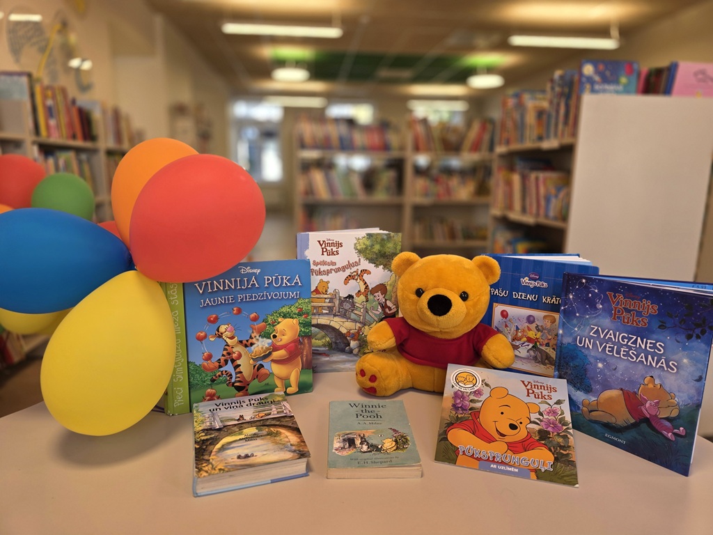 Bibliotēkas grāmatu izstāde ar Vinnija Pūka grāmatām, mīksto rotaļlietu un krāsainiem baloniem