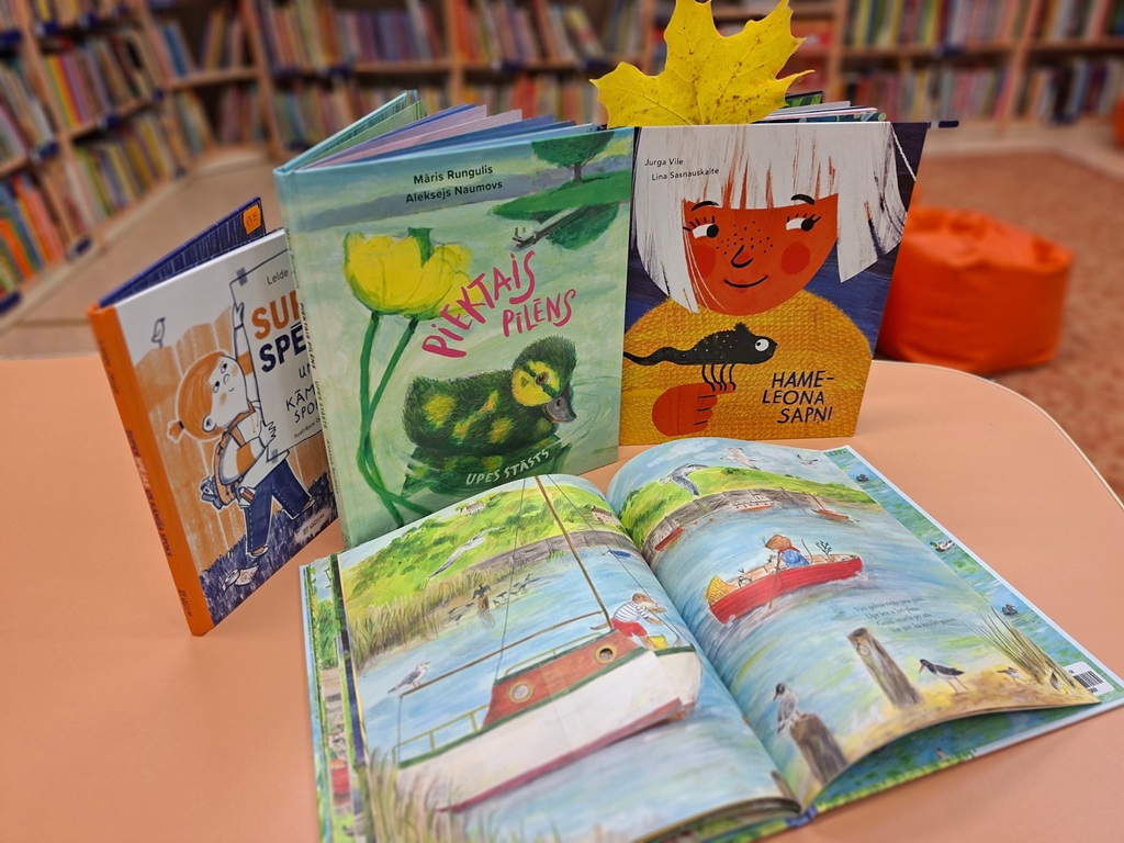 Bibliotēkas grāmatu izstāde ar bērnu grāmatām un atvērtu ilustrētu grāmatu uz galda