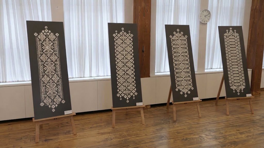 Četri stendi uz koka statīviem gaišā telpā ar baltiem aizkariem